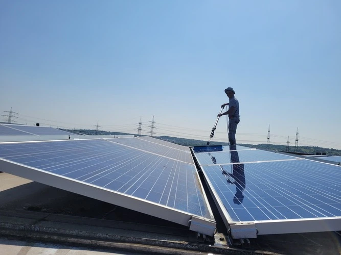 A VONPRO technician using a telescopic carbon pole with a rotating soft brush and an osmosis water supply on a residential roof.